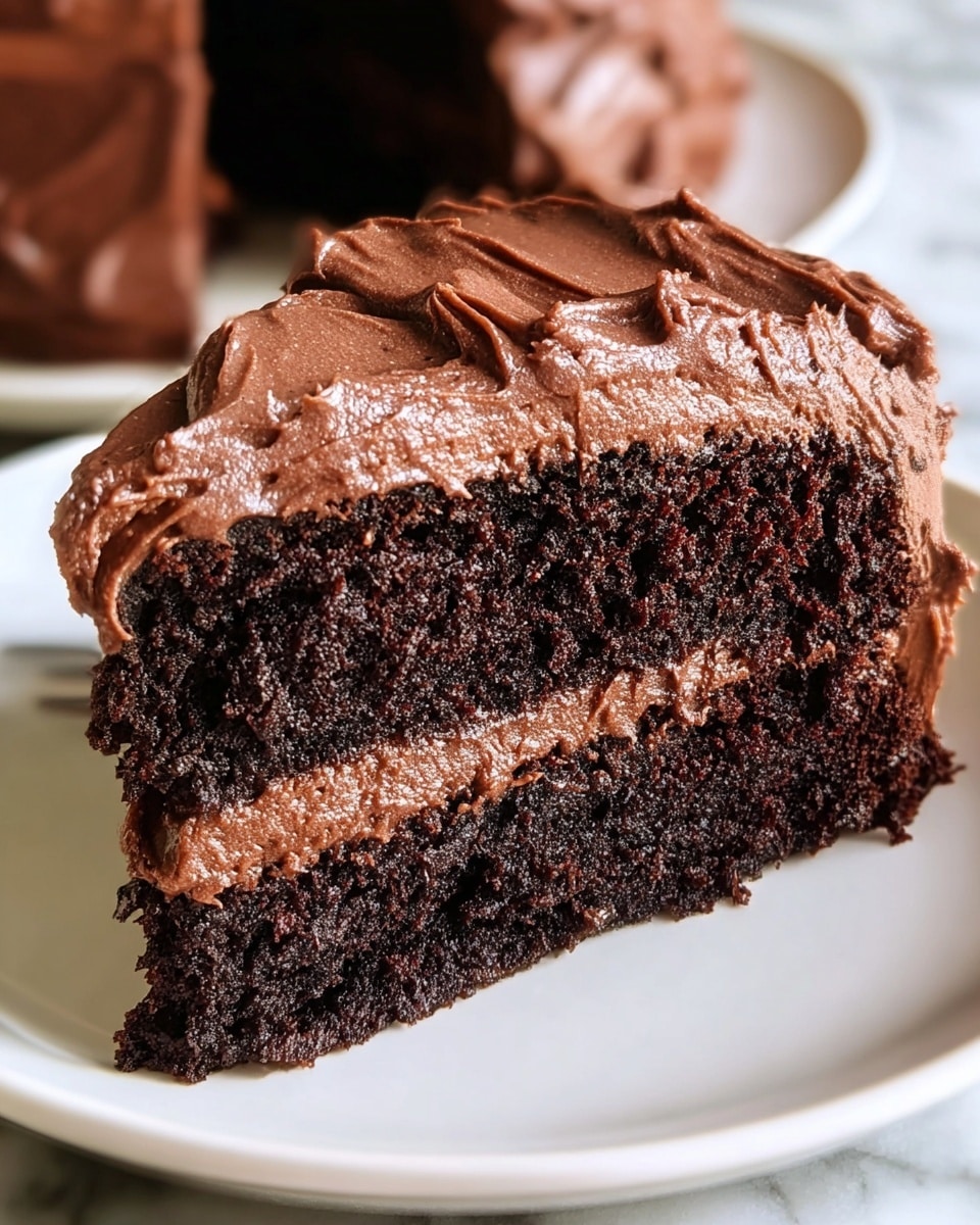 A close-up view of a two-layer chocolate cake slice on a white plate, placed on a white marbled surface. The bottom layer is dark, moist chocolate cake with a dense texture. The middle layer is a rich, smooth milk chocolate frosting spread evenly. The top layer is another dark chocolate cake slice covered thickly with shiny, whipped chocolate frosting that has visible swirls and soft peaks, showing a creamy texture. Photo taken with an iphone --ar 4:5 --v 7