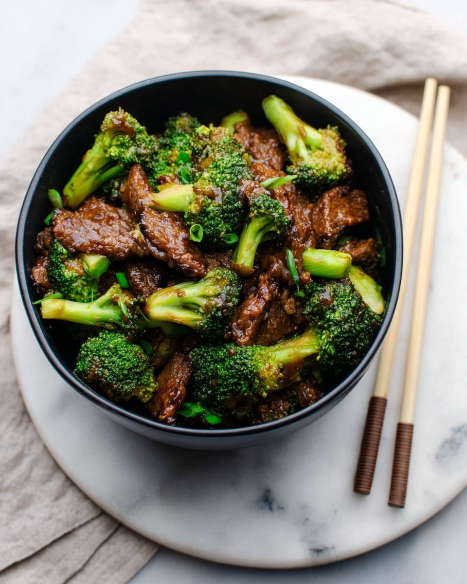 A black bowl filled with several pieces of bright green broccoli mixed with dark brown saucy beef chunks, creating a rich contrast between the fresh vegetable and glazed meat. The broccoli florets are chunky and slightly glossy, scattered evenly with the tender beef that has a textured surface showing the sauce. The bowl is placed on a round white plate with a smooth surface, resting on a white marbled textured surface. To the side of the plate, there is a pair of light wood chopsticks with dark tips, adding a simple but elegant touch to the setting. photo taken with an iphone --ar 4:5 --v 7