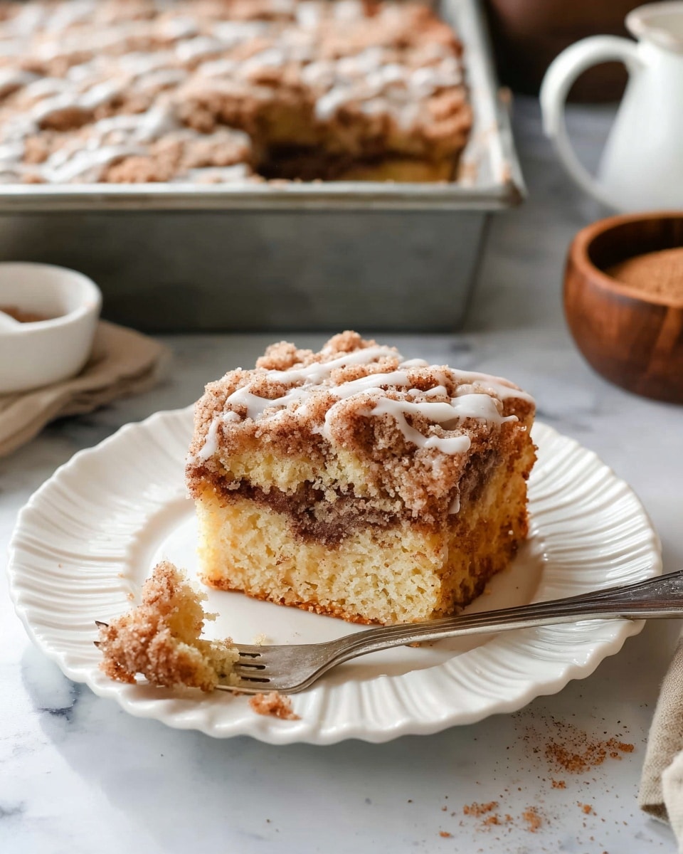 A white scalloped plate holds a thick slice of crumb cake with two visible layers: a light golden yellow base with a middle swirl of dark cinnamon-brown filling, topped with a rough-textured crumb layer covered in a white glaze drizzle. A piece of the cake is cut and placed near the slice on the plate, showing the soft crumb inside. A silver fork rests beside it, holding a bite of the cake. In the background, a metal baking pan filled with more crumb cake is visible, along with a white bowl of cinnamon sugar and a wooden bowl of brown sugar on a white marbled texture. photo taken with an iphone --ar 4:5 --v 7