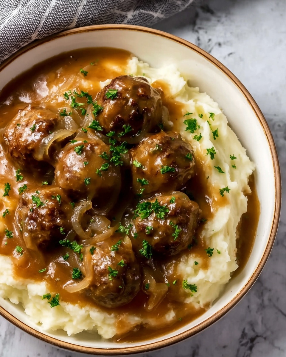 A bowl with two main layers is shown; the bottom layer is smooth, creamy mashed potatoes in a soft off-white color. On top, there is a thick layer of brown gravy with visible translucent cooked onions, covering multiple round meatballs that look juicy and tender. The dish is sprinkled with small green bits of fresh parsley, adding a touch of color contrast. The bowl is white with a thin brown rim, placed on a white marbled surface photo taken with an iphone --ar 4:5 --v 7