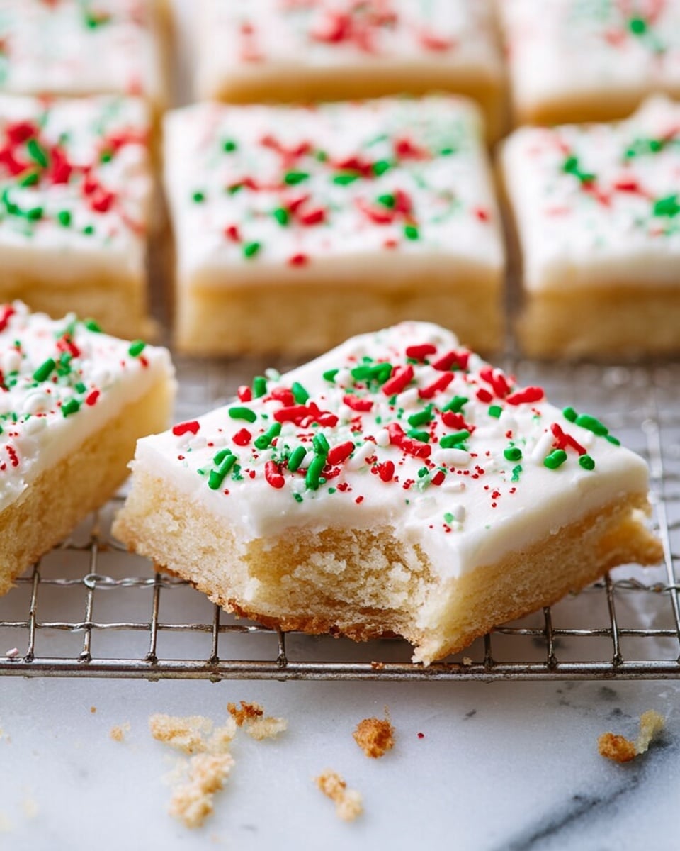 The image shows several square sugar cookie bars on a metal cooling rack placed on a white marbled surface. Each bar has two visible layers: a thick, light golden brown base with a soft, crumbly texture, and a smooth white frosting layer on top. The frosting is decorated with red and green sprinkles scattered evenly across the surface. One cookie bar in the front has a bite taken out of it, showing the soft inside of the base layer. Some sprinkles and crumbs are scattered on the white marbled surface around the rack. photo taken with an iphone --ar 4:5 --v 7