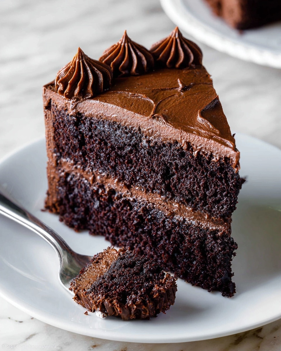 A slice of rich chocolate cake with two thick, dark brown layers of moist cake separated by a smooth, darker chocolate frosting layer. The top of the slice is covered with an even layer of chocolate frosting with textured swirls, and six small dollops of glossy chocolate frosting sit along the back edge. The slice rests on a white plate with a small fork holding a bite-sized piece of the cake in the foreground. The scene has a white marbled texture surface beneath the plate. photo taken with an iphone --ar 4:5 --v 7