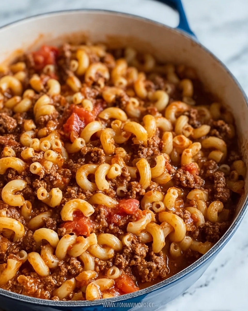 The image shows a close-up of a large white pot filled with a hearty mix of elbow macaroni pasta and ground meat cooked in a tomato sauce. The macaroni pieces are light yellow and slightly glossy, scattered evenly throughout the dish, while the ground meat is brown and crumbly, covering much of the pasta. Bright red chunks of tomato add spots of color mixed within the pasta and meat. The sauce looks thick and rich, coating all the ingredients but allowing the pasta and meat to hold their textures. The white pot is set on a surface with a white marbled texture. Photo taken with an iphone --ar 4:5 --v 7