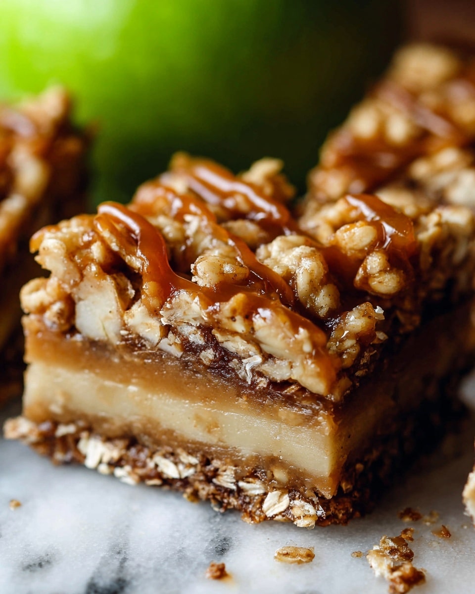 The image shows a close-up of a square dessert bar with four visible layers. The bottom layer is dark brown, textured like a firm crust mixed with oats. Above that is a lighter tan layer with a smooth and slightly dense texture, followed by a thin, paler cream-colored layer. The top layer is a crunchy oat and nut mixture, golden brown with a sticky glossy caramel drizzle and tiny white flakes sprinkled on it. In the blurry background, a green apple is partially visible, all set on a white marbled texture. photo taken with an iphone --ar 4:5 --v 7
