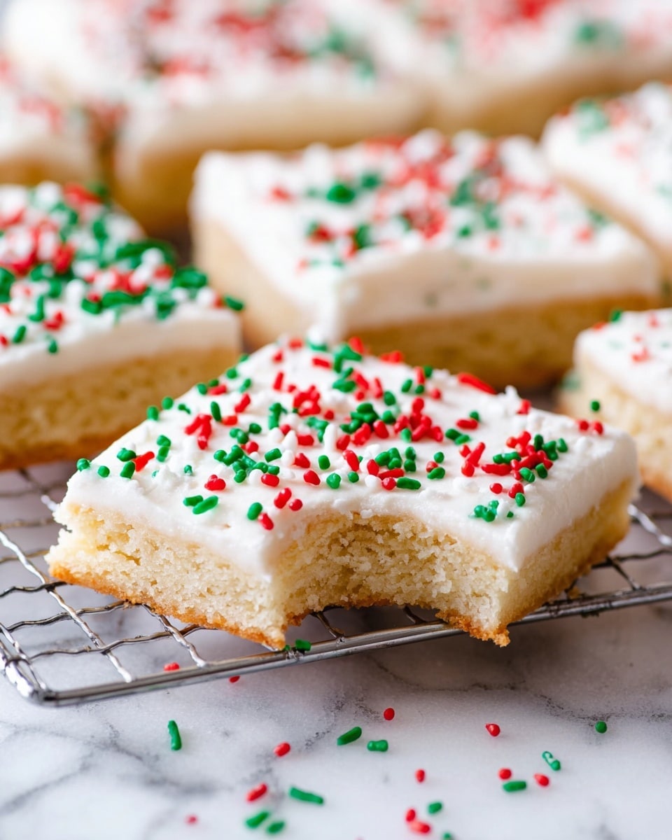 The image shows a close-up of several square sugar cookie bars arranged on a wire rack over a white marbled surface. Each bar has two layers: the bottom layer is a light golden, soft cookie base with a visible crumb texture, and the top layer is a thick, smooth white frosting. The frosting is decorated with red and green sprinkles scattered evenly across the surface. One cookie bar in the front has a bite taken out, showing the soft cookie texture inside. Some sprinkles are also scattered on the white marbled surface beneath the rack. Photo taken with an iphone --ar 4:5 --v 7
