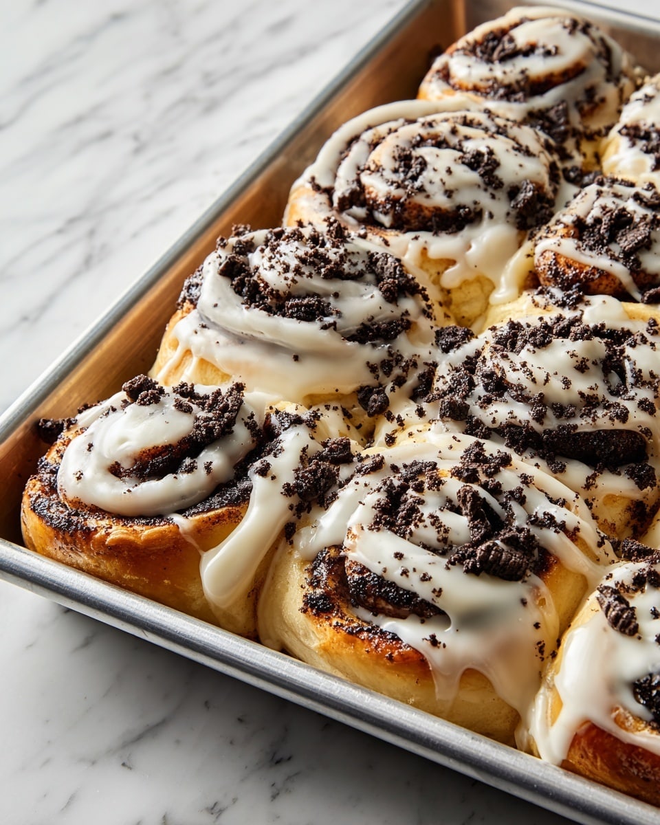 A tray of cinnamon rolls is shown from above, each roll having multiple thick layers of golden-brown dough swirled with dark chocolate or cookie crumb filling. The rolls are generously drizzled with smooth white icing that flows over the swirls, adding a creamy texture. Crushed dark cookie bits are sprinkled over the icing, adding a crumbly, crunchy detail on top. The tray is silver metal, resting on a white marbled surface. photo taken with an iphone --ar 4:5 --v 7