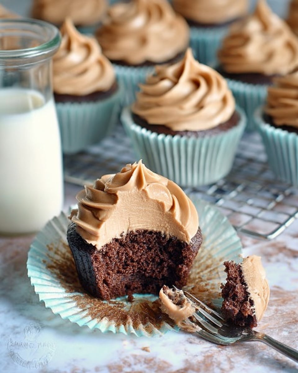 The image shows a chocolate cupcake with two visible layers: the bottom layer is dark, moist chocolate cake with a soft texture, and the top layer is a swirled, light brown creamy frosting with a smooth texture, sitting generously on top in a spiral shape. One cupcake has a bite taken out of it, showing the cake inside, and a small piece of the cupcake with some frosting is placed in front on a silver fork. The cupcake liner is light blue with a slightly crinkled edge. In the background, multiple cupcakes with the same frosting swirl are arranged on a metal cooling rack. To the left, there is a clear glass jug filled with milk, all resting on a white marbled texture. photo taken with an iphone --ar 4:5 --v 7