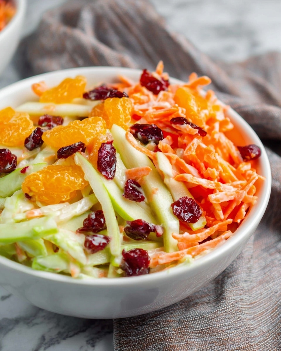 A white bowl filled with a colorful salad showing three main layers: the bottom layer has thin pale green slices of apple, the middle layer contains bright orange shredded carrots, and the top layer is decorated with small pieces of dark red dried cranberries and vibrant orange mandarin segments, all lightly coated in a creamy dressing. The texture looks fresh and crispy with a mix of smooth and firm elements. The bowl sits on a white marbled surface, with a gray cloth softly blurred in the background. Photo taken with an iphone --ar 4:5 --v 7
