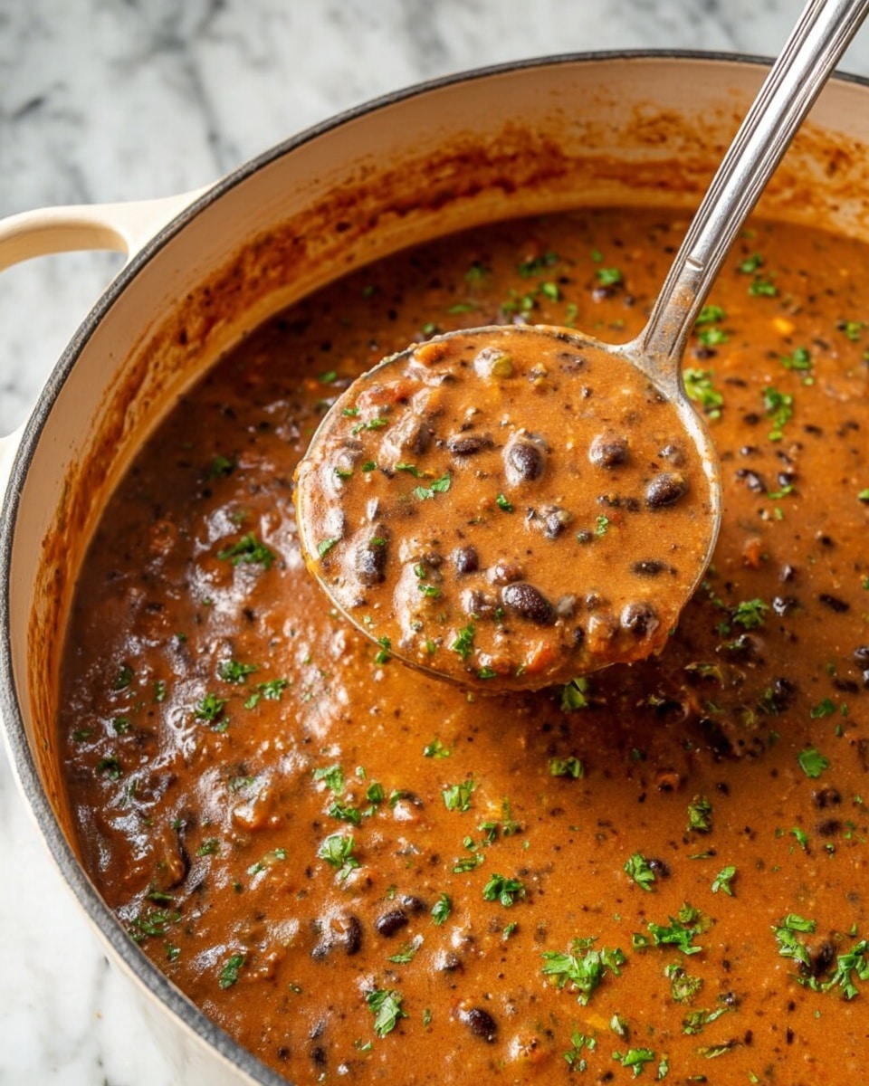 A thick, creamy stew with a reddish-brown color fills a large pot with light beige interior, showing visible bits of black beans and small chunks of vegetables throughout. Bright green chopped herbs are sprinkled on top, adding contrast to the rich sauce. A large silver ladle lifts a scoop of the stew, displaying its dense texture with tiny flecks of black and green spread evenly inside the ladle. The pot sits on a white marbled surface. photo taken with an iphone --ar 4:5 --v 7
