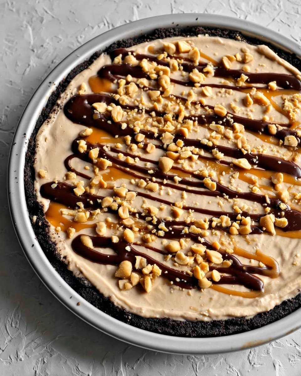 A dessert with three visible layers in a round white metal pan is shown. The base layer is a dark crumbly crust, almost black in color, which holds a thick middle layer of smooth light beige cream spread evenly. On top, chopped peanuts are scattered all over, adding a rough texture and light yellow color. The dessert is drizzled with dark brown chocolate sauce and caramel sauce in thin, irregular lines. The background surface has a white marbled texture. photo taken with an iphone --ar 4:5 --v 7