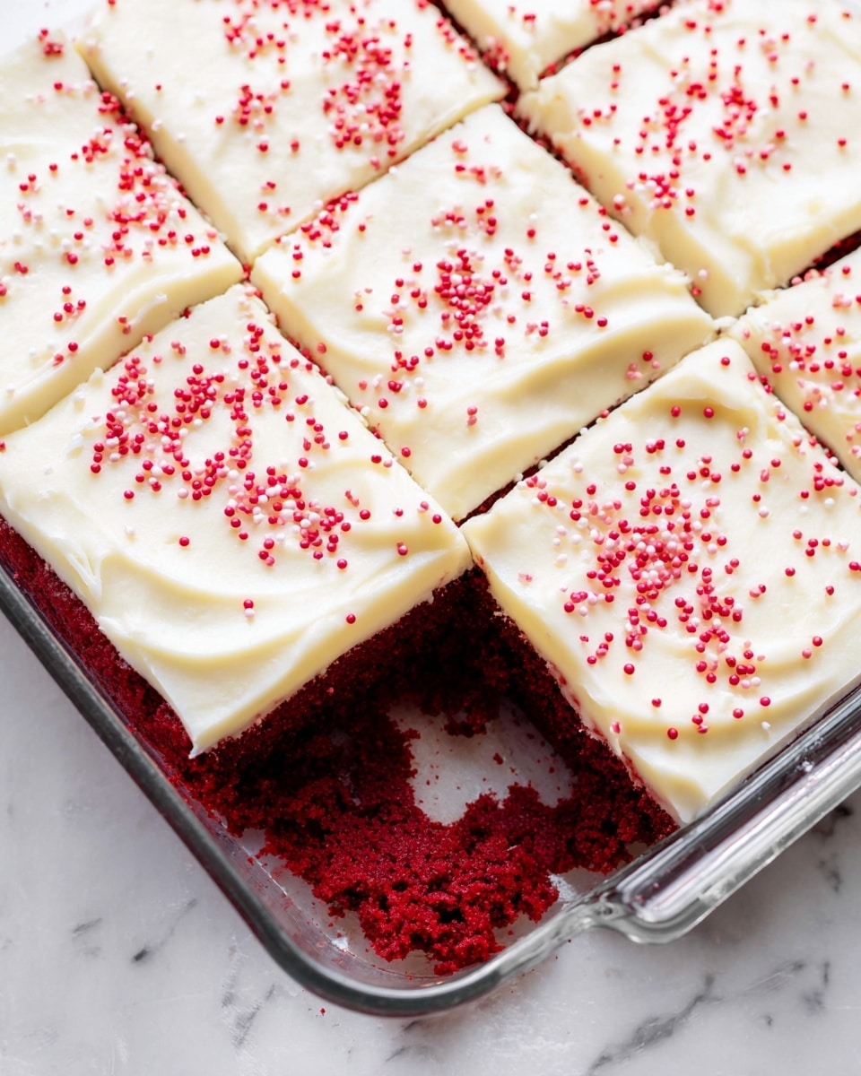 A close-up view of a rectangular glass baking dish containing red velvet cake cut into six square pieces, showing two layers: a bottom layer of rich, deep red cake with a soft texture, and a top layer of thick, creamy white frosting that is smooth with gentle swirls. The frosting is sprinkled with small, round red sprinkles scattered evenly over each square. One piece is slightly pulled out, revealing the moist crumb of the cake. The dish is placed on a white marbled surface, and the scene is bright and clear. Photo taken with an iphone --ar 4:5 --v 7