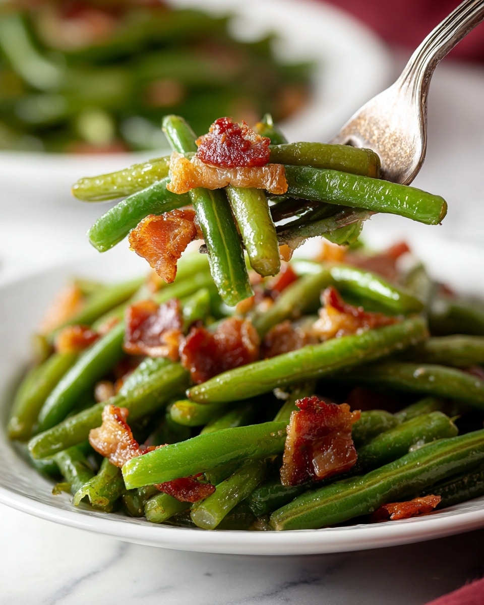 A white plate is filled with cooked green beans, coated in a light glossy sauce that makes them look tender. Scattered on top and mixed inside are crispy pieces of golden-brown bacon, adding texture and rich color contrast. A silver fork lifts a small bundle of green beans and bacon pieces above the plate, showing the dish’s layered effect clearly. The background is soft and blurred with a white marbled surface underneath the plate, emphasizing the dish’s vibrant green and warm brown tones. photo taken with an iphone --ar 4:5 --v 7