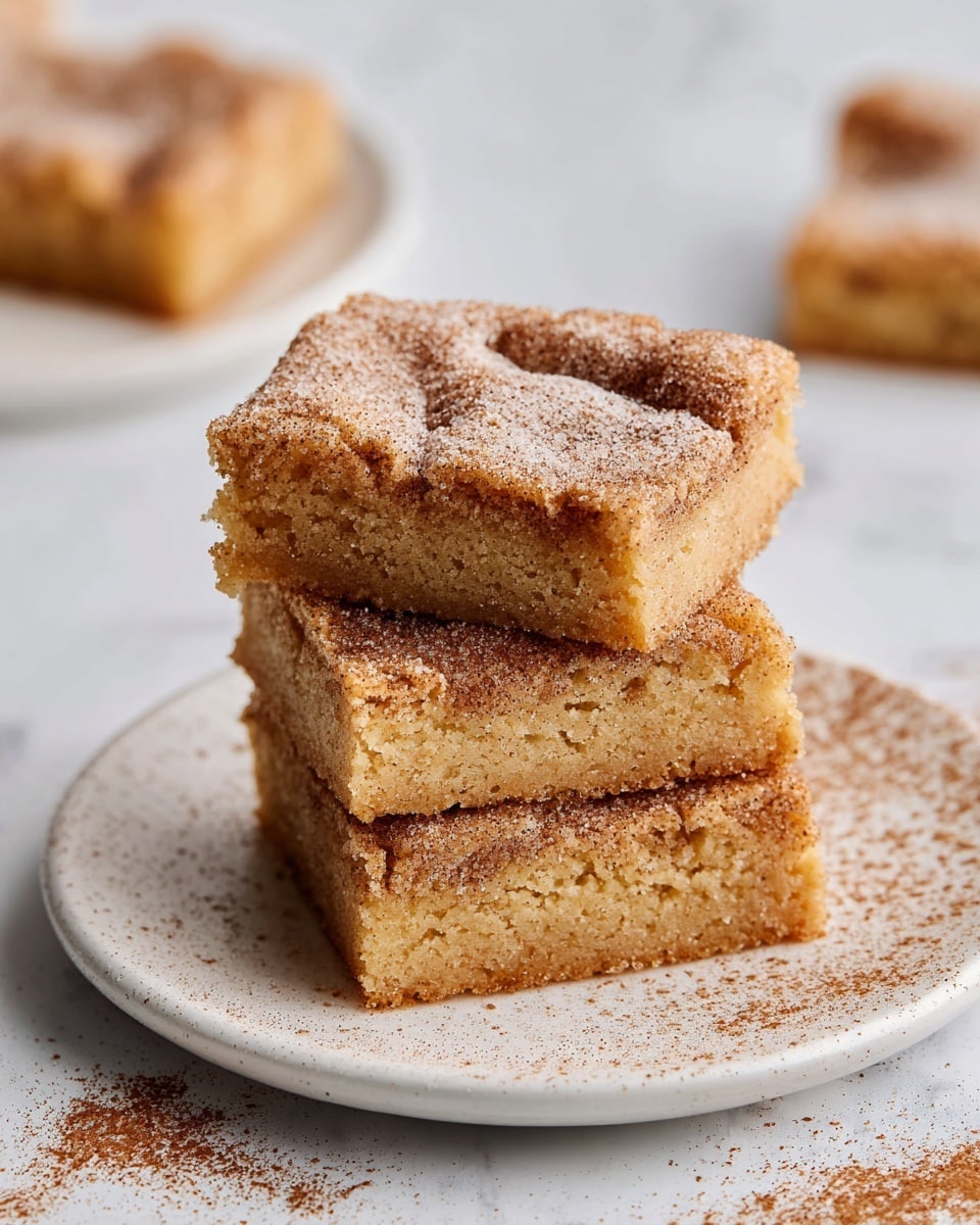 A stack of three square blondies with a light brown color and soft, crumbly texture sits on a white plate. Each blondie is topped with a generous layer of cinnamon sugar, creating a speckled pattern of darker brown on the surface. The top blondie has a slight indentation in the center, showing its tender and moist inside. The plate rests on a white marbled surface, with a light dusting of cinnamon sugar scattered around. In the background, there are two more blondies blurred out, adding depth to the image. Photo taken with an iphone --ar 4:5 --v 7