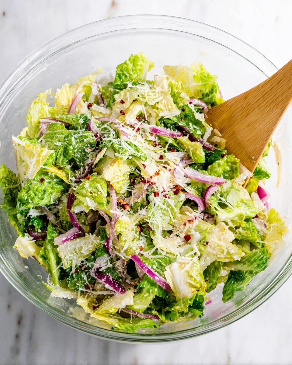 A clear glass bowl filled with fresh salad showing a mix of green and pale yellow lettuce leaves torn into medium pieces as the base layer, topped with thin slices of purple and white onion scattered evenly throughout. Small, fine shreds of white cheese are sprinkled over the top, along with tiny red chili flakes adding a hint of red. A light wooden spatula is placed inside the bowl on the right side, partly resting on the salad. The bowl sits on a white marbled surface, bright and clean, with natural lighting highlighting the colors and textures of the ingredients. Photo taken with an iphone --ar 4:5 --v 7