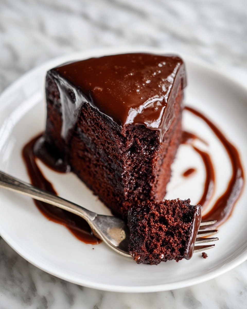 A thick slice of dark chocolate cake sits on a white plate with a glossy, smooth chocolate ganache coating the top and sides, dripping slightly down the edges. The cake appears moist and dense with a rich texture. A fork rests beside the slice, holding a bite-sized piece of the cake, which also shows the deep chocolate color and crumbly texture. There are artistic swirls of chocolate sauce on the plate around the cake, and the scene is set on a white marbled texture. photo taken with an iphone --ar 4:5 --v 7