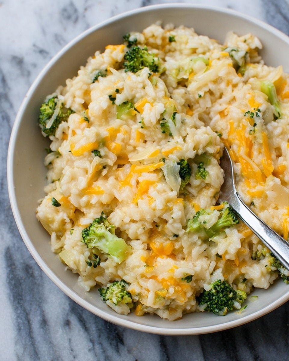 A close-up view of a creamy rice dish served in a white bowl, showing a mix of cooked white rice, small green broccoli florets, and thin strands of melted orange cheese evenly spread throughout. The rice is soft and moist with a slightly shiny texture, and there are bits of cooked onion adding light translucent spots. A metal spoon is partially buried in the bowl, positioned diagonally from the top right. The background is a white marbled surface. photo taken with an iphone --ar 4:5 --v 7