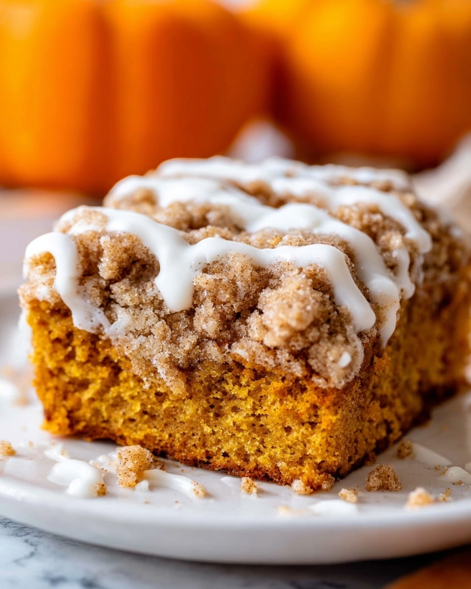 A close-up of a single piece of crumb cake with two visible layers: the bottom layer is a dense, moist orange-brown cake, and the top layer is a thick, crumbly, golden-brown streusel topping with a rough texture. White icing is drizzled unevenly over the streusel, adding a smooth contrast. Some crumbs and small icing spots are scattered on the white plate around the cake. The background shows blurred orange pumpkins against a white marbled surface. photo taken with an iphone --ar 4:5 --v 7