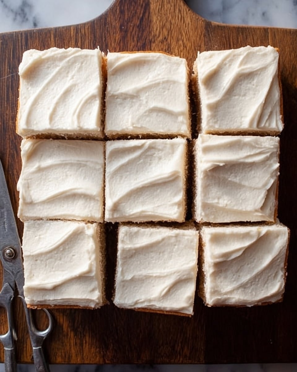 A square cake cut into nine pieces sits on a dark wooden board, each piece topped with a thick, smooth layer of creamy white frosting that has gentle, wavy textures. The cake underneath has a light brown color, showing through the gaps between pieces. A pair of old kitchen scissors rests next to the bottom left corner of the cake. The background is a white marbled texture. photo taken with an iphone --ar 4:5 --v 7