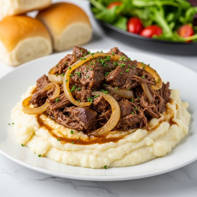 A white plate holds a base layer of creamy, smooth mashed potatoes with a light, fluffy texture and soft white color. On top, there is a thick layer of dark brown braised beef, shredded and tender, mixed with translucent, cooked onion slices. The beef and onions are coated in a glossy, rich brown gravy, sprinkled with chopped green herbs for garnish. The plate sits on a surface with a white marbled texture, and in the blurred background, there is a black dish with green leafy salad and small red tomatoes, along with two light brown bread rolls. Photo taken with an iphone --ar 4:5 --v 7