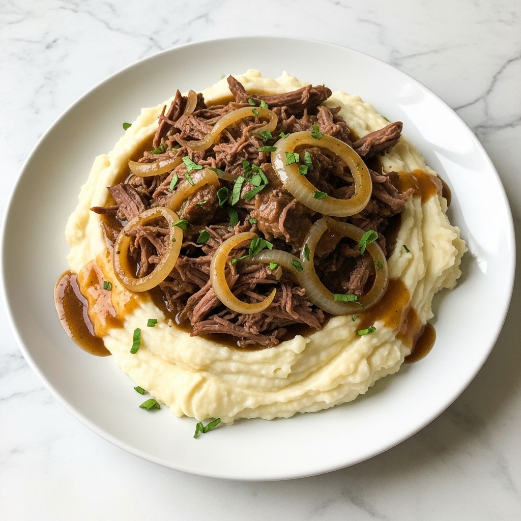 A white plate holds a bed of smooth, creamy mashed potatoes as the bottom layer, which is thick and spread out evenly covering the plate's center. On top, there is a large serving of shredded, brown pot roast meat mixed with translucent cooked onion slices. The meat looks tender and juicy, coated in glossy brown gravy that slightly drips down the sides onto the mashed potatoes. Small green herb pieces are sprinkled over the dish, adding a fresh contrast. The plate is placed on a white marbled surface. Photo taken with an iphone --ar 4:5 --v 7