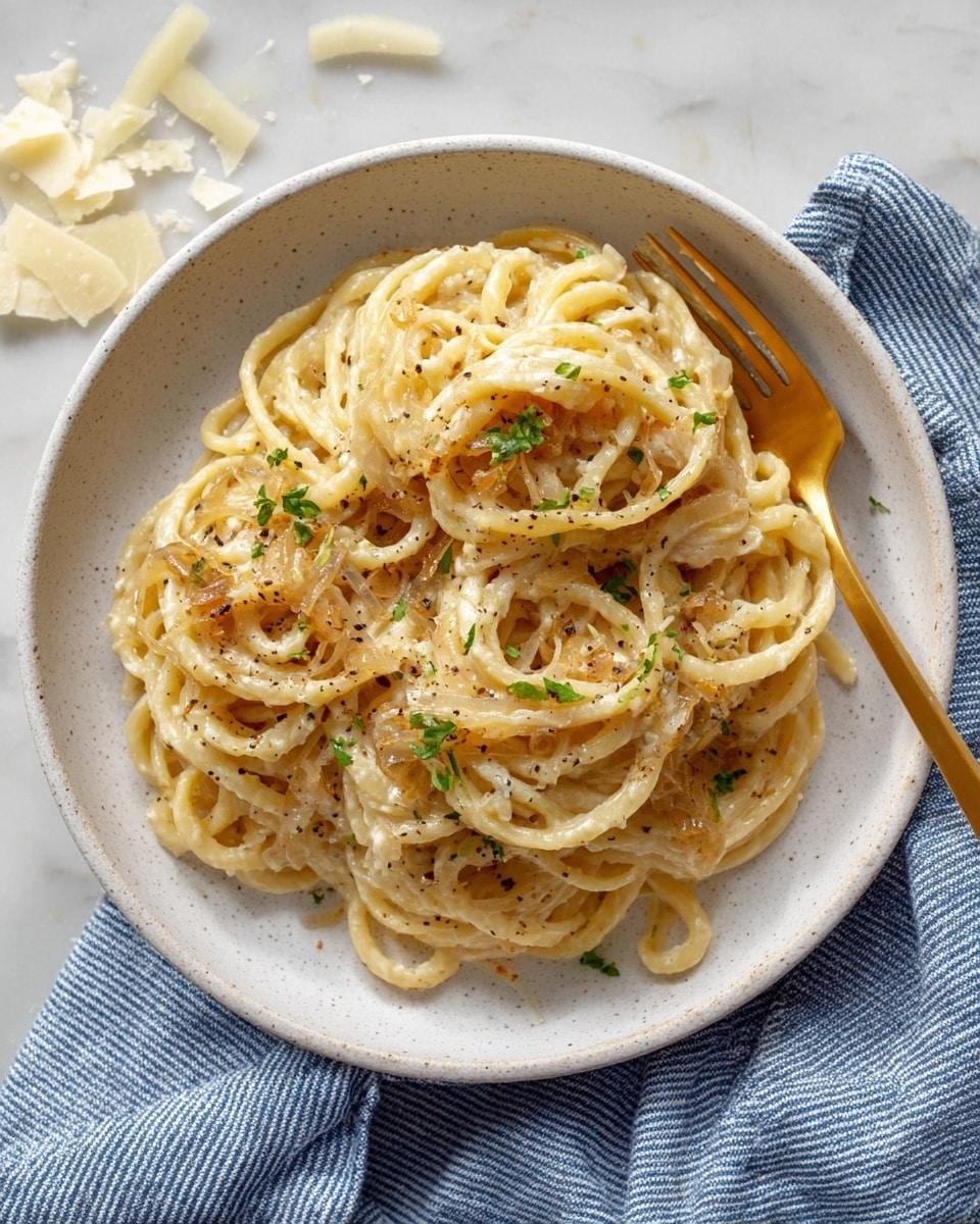 The image shows a close-up of a silver pan filled with creamy pasta mixed with caramelized onions. The pasta is light beige with a smooth texture, and the onions are soft with a golden brown color, evenly mixed throughout. Some small green herb bits are scattered on top, adding a touch of color. A pair of silver tongs is placed inside the pan, partially lifting the pasta. The pan sits on a white marbled surface with a blue and white striped cloth underneath. photo taken with an iphone --ar 4:5 --v 7