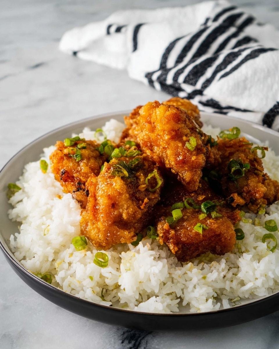 The dish shows a single white plate on a white marbled surface, filled with a base layer of fluffy white rice spread evenly across the plate. On top of the rice, there are four pieces of golden brown fried chicken, each piece crispy with a rough textured coating and slightly darker brown spots from frying. Small pieces of green onion are sprinkled lightly over the chicken and rice, adding a touch of color contrast. In the background, a white napkin with black stripes is softly folded. photo taken with an iphone --ar 4:5 --v 7