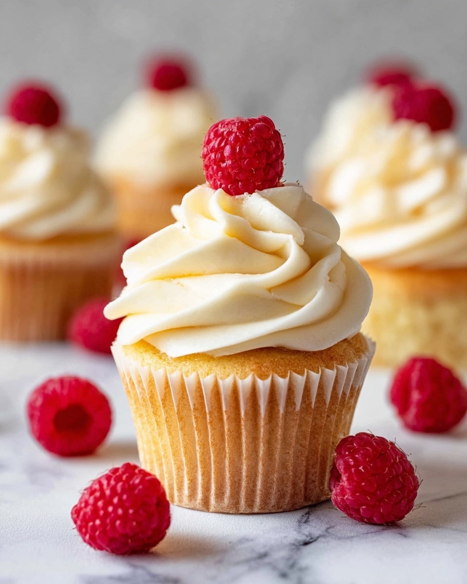 The image shows a close-up of a cupcake being decorated with creamy, light beige frosting. The cupcake has one visible layer of golden yellow cake at the base, wrapped in a white paper liner. Swirls of smooth frosting are being piped from a metal piping tip on top, forming multiple textured and curved layers that rise to a peak. In the background, there are three more cupcakes, two with similar frosting swirls and one plain cupcake without frosting, all placed on a surface with a white marbled texture. Photo taken with an iphone --ar 4:5 --v 7