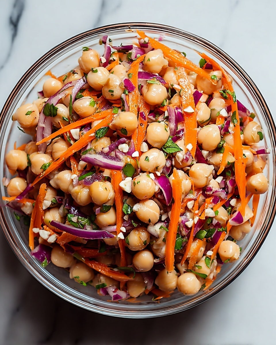 A clear white bowl filled with a colorful salad layered with round, light beige chickpeas scattered throughout. Thin strips of bright orange carrots and small pieces of chopped purple-red onions add texture and color, mixed with small green herb leaves. The salad has a glossy finish, suggesting a light dressing, with some tiny white bits that look like nuts or seeds sprinkled on top. The bowl is placed on a surface with a white marbled texture, highlighting the vibrant colors inside. photo taken with an iphone --ar 4:5 --v 7