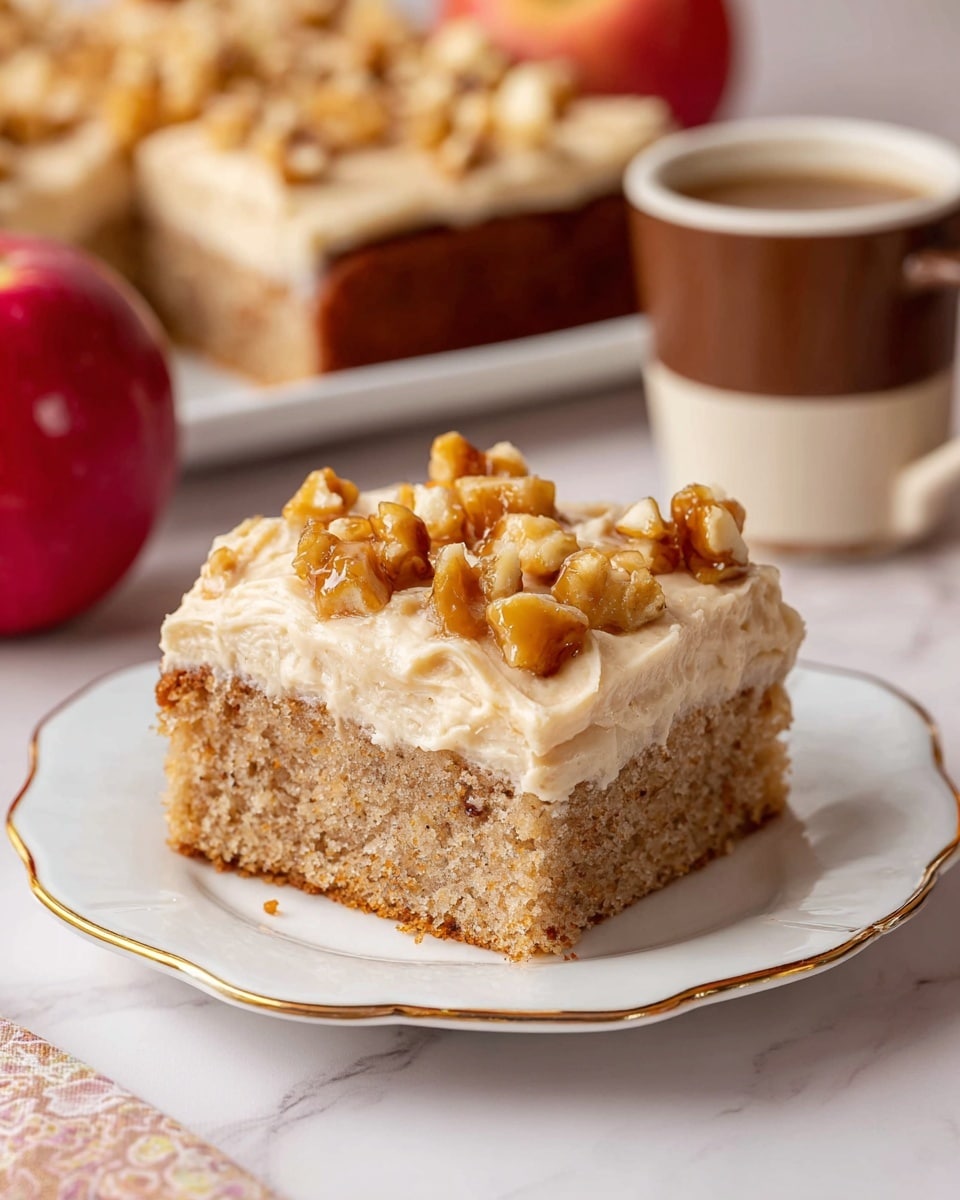 A square piece of cake sits on a white plate with a scalloped edge and gold trim. The cake has two layers: a moist, light brown spongy base and a thick, creamy light beige frosting layer on top. The frosting is topped with small chunks of golden-brown caramelized nuts scattered evenly. In the background, the rest of the cake is visible with the same layers and topping, along with a red apple to the left and a two-tone brown mug with a handle to the right, all placed on a white marbled surface. Photo taken with an iphone --ar 4:5 --v 7