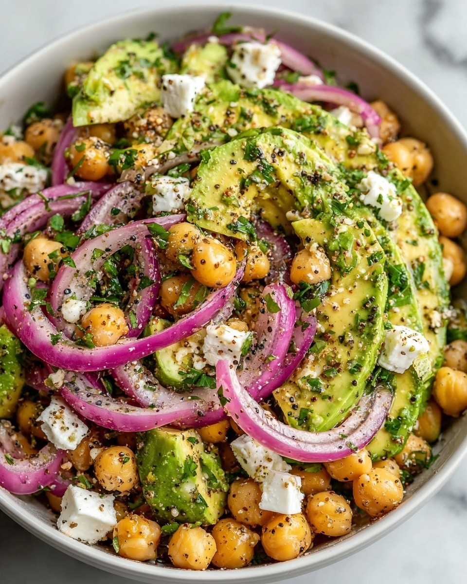 This dish is a colorful salad served in a white bowl on a white marbled surface. The salad has three main layers: the bottom layer has round beige chickpeas, the middle layer features bright green chunks of avocado with a creamy texture, and the top layer is made of thin, curved slices of purple-red onion. Scattered throughout are small white cubes of cheese, adding contrast to the colors. The salad is sprinkled with finely chopped green herbs and a seasoning mix with visible black seeds and ground spices, giving it a speckled texture. photo taken with an iphone --ar 4:5 --v 7