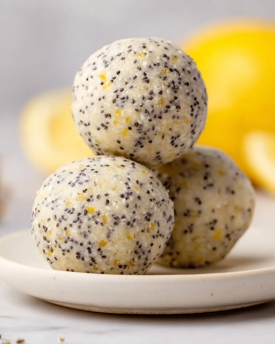 This image shows a close-up of three round energy balls stacked on a white plate with a smooth surface. The balls are pale cream in color and have many small black poppy seeds and tiny white seeds held within the soft texture. There are also small yellow specks spread evenly inside the balls. The background has a white marbled texture and a blur of yellow lemon wedges can be seen in the distance. Photo taken with an iphone --ar 4:5 --v 7