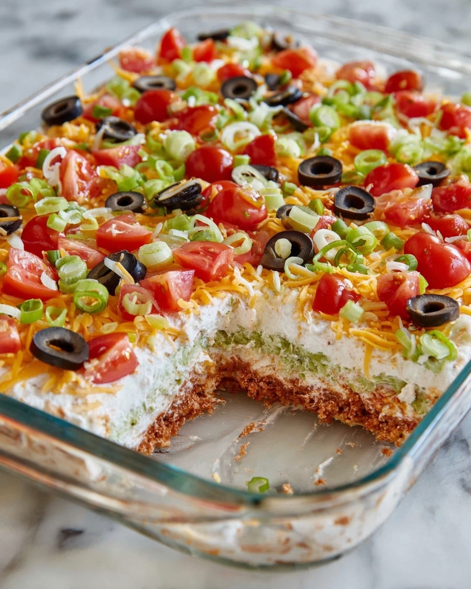 A clear rectangular glass dish holds a multi-layered dip with a missing corner piece showing distinct layers: a bottom creamy beige base, a middle green layer with chunky texture, followed by a smooth pale layer topped with a mix of shredded yellow and white cheese. The top is decorated with scattered small red tomato pieces, black olive slices, and thinly sliced green onions. The dish is placed on a white marbled surface. Photo taken with an iphone --ar 4:5 --v 7