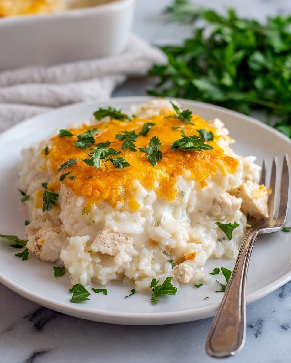 A white baking dish filled with a creamy baked rice casserole topped with a golden brown crust of melted cheese sprinkled with chopped green parsley leaves. A wooden spoon lifts a scoop showing the layers of soft white rice mixed with tender, browned chicken pieces, all covered in a rich, slightly stretchy cheese sauce. The background features a white marbled surface and a blurred green plant, adding freshness to the warm, comforting dish. photo taken with an iphone --ar 4:5 --v 7